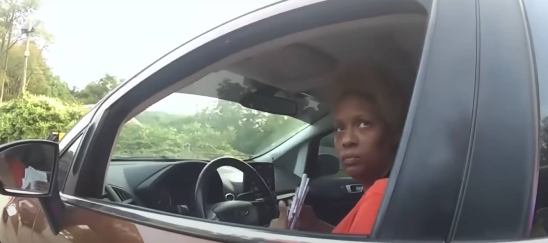 Woman seen from inside car, looking out with window rolled down.