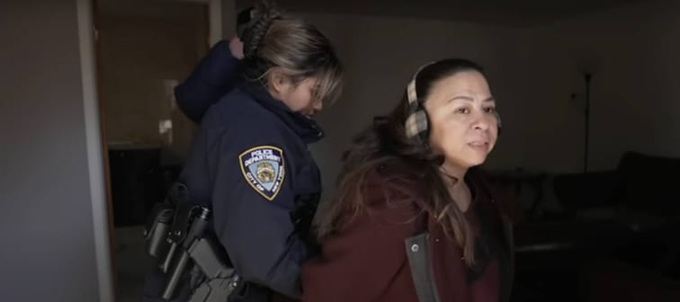 Woman wearing headphones looks distressed as being led off by police in handcuffs.